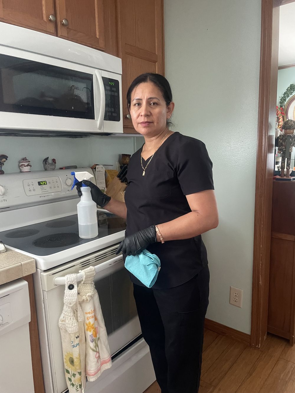 A Blandina cleaner in a client kitchen holding a spray bottle and microfiber cloth beside a cleaned cooktop.